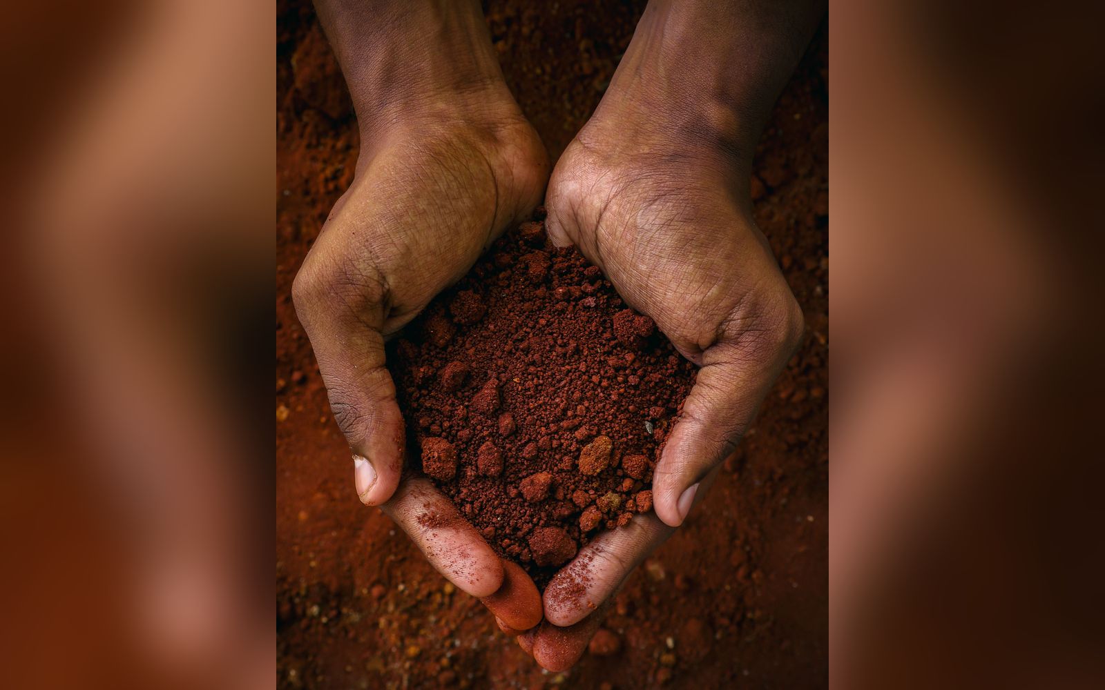 Mains tenant de la terre latéritique rouge, matière première de l'activité minière guinéenne